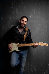 Músico sosteniendo una guitarra eléctrica en un fondo oscuro