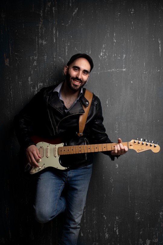 Músico sosteniendo una guitarra eléctrica en un fondo oscuro