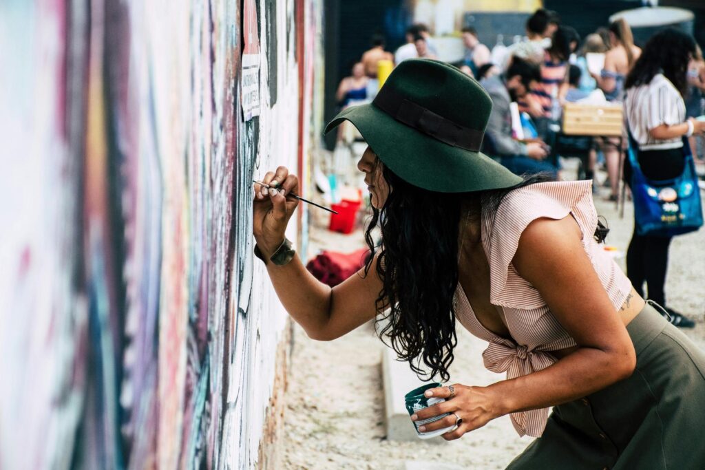 Mujer pintando un mural en un evento cultural al aire libre.