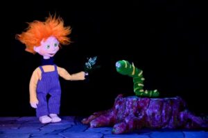 Marioneta con cabello naranja interactuando con un gusano verde