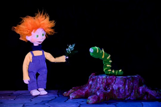 Marioneta con cabello naranja interactuando con un gusano verde