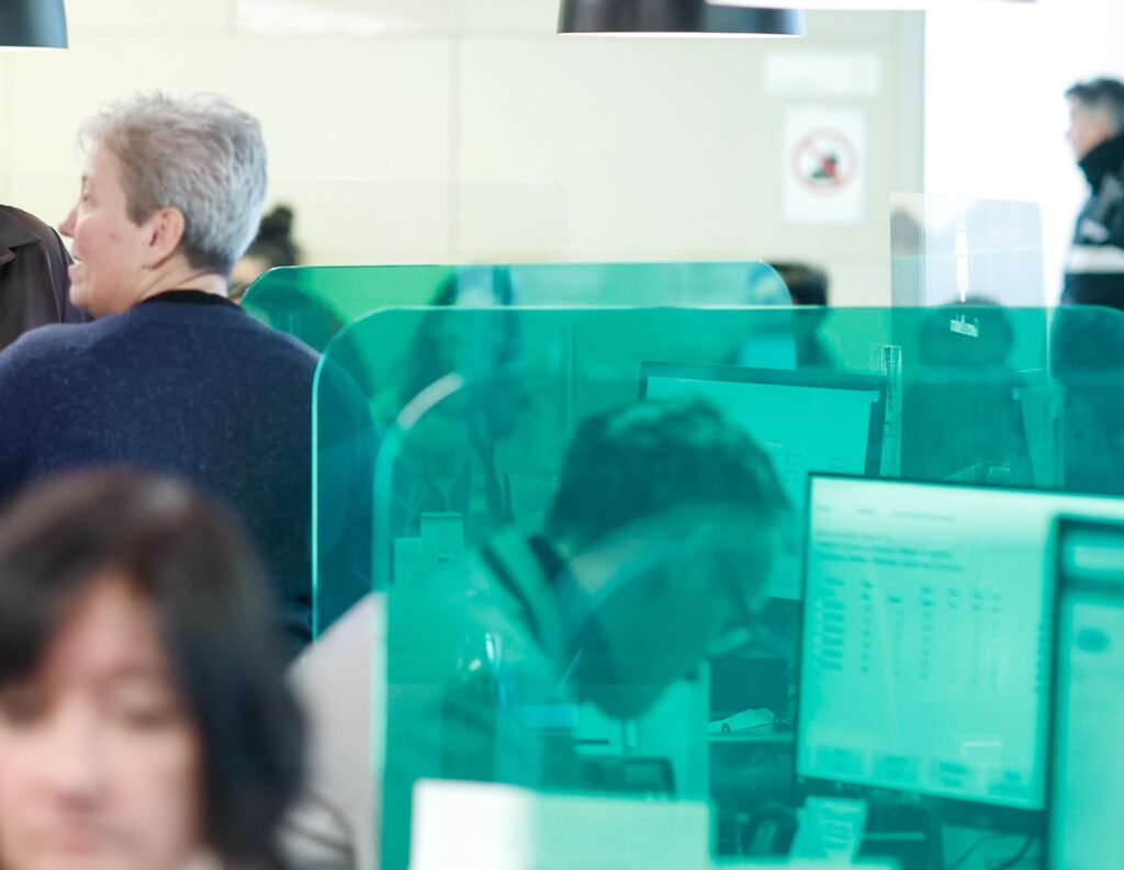 Personas en un entorno de oficina con pantallas de computadora y paneles de vidrio.