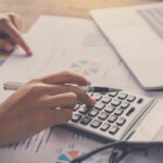 Persona utilizando una calculadora sobre documentos de auditoría y gráficos