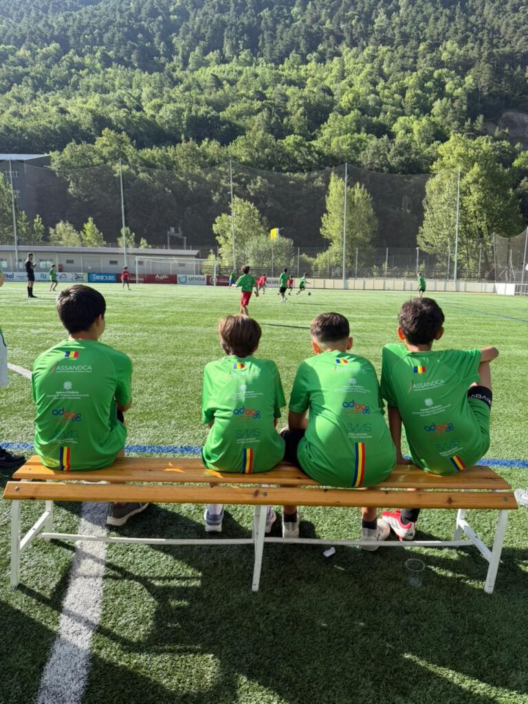 Jóvenes sentados en un banco durante un partido de fútbol en un proyecto educativo.