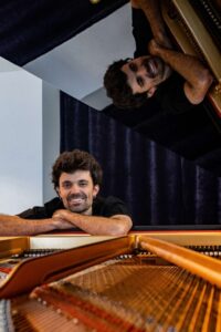 Kic Barroc sonriente junto a un piano en un entorno musical.