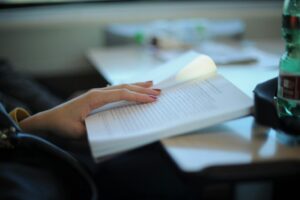 Persona leyendo un libro en una mesa con una botella de agua.