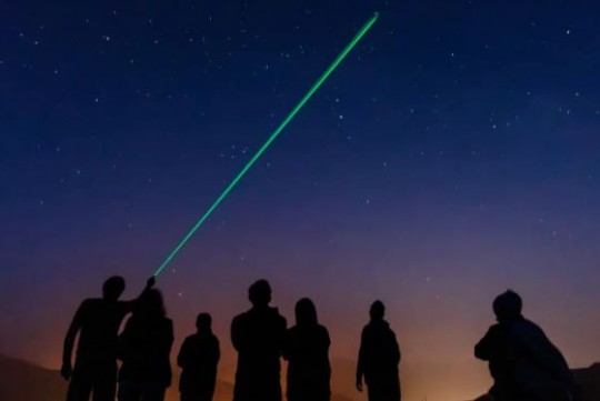 Grupo de personas observando estrellas con un láser verde en el cielo nocturno