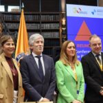 Cuatro asistentes posan ante banderas y una pantalla de una reunión sobre protección civil.
