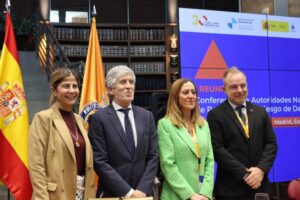 Cuatro asistentes posan ante banderas y una pantalla de una reunión sobre protección civil.
