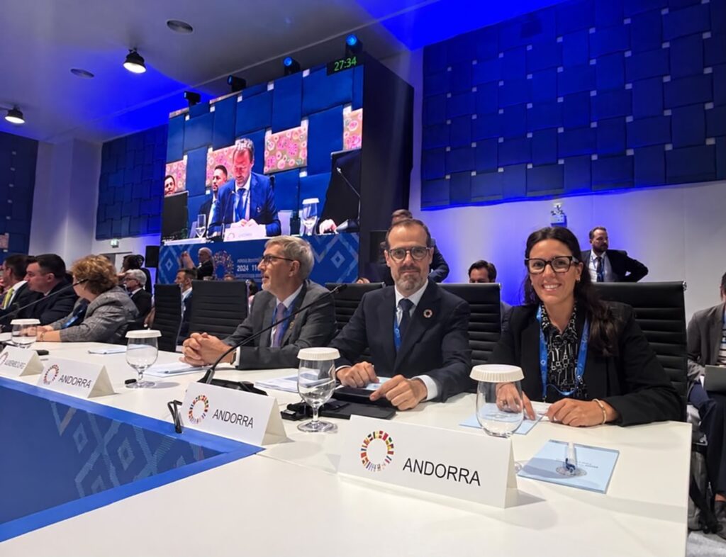 Personas sentadas ante una mesa de reunión con carteles de Andorra en primer plano