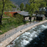 Edificios de piedra junto a un río, rodeados de árboles y montañas.