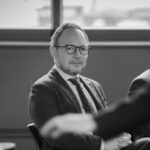Hombre con gafas sentado en una sala, en fotografía en blanco y negro