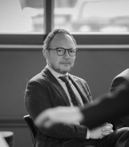 Hombre con gafas sentado en una sala, en fotografía en blanco y negro