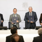 Cuatro hombres muestran carpetas ante el emblema del Govern d’Andorra.
