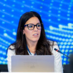 Lorena Jordana sentada ante un portátil y un micrófono, con un cartel de Andorra