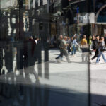 Peatones caminan frente a escaparates, reflejados en los cristales de una calle comercial.