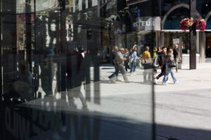 Peatones caminan frente a escaparates, reflejados en los cristales de una calle comercial.