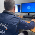 Agente de espaldas con chaleco de INTERPOL Andorra frente a varias pantallas.