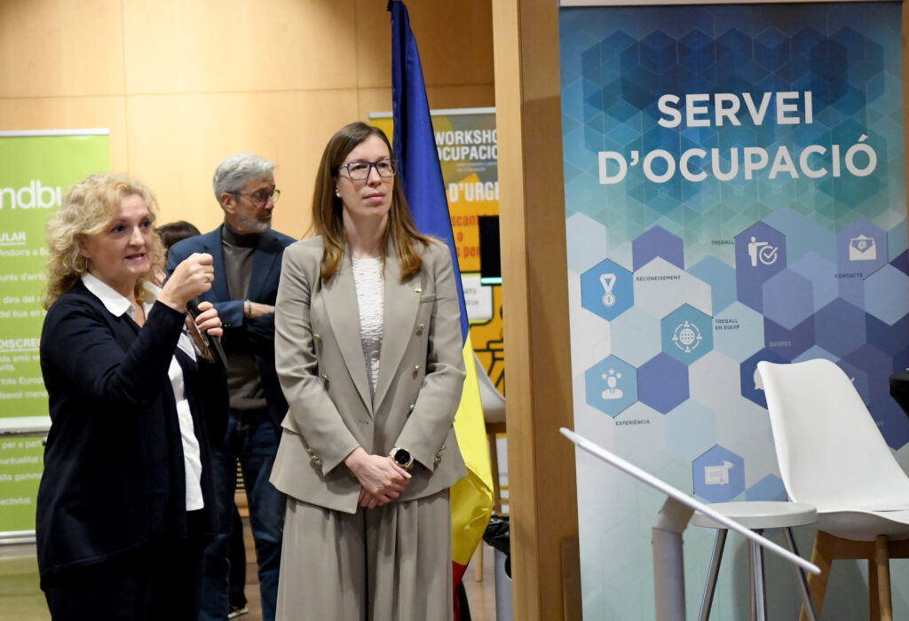Una mujer sostiene un micrófono junto a otra persona frente al cartel del Servei d’Ocupació.