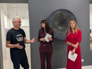 Tres personas están de pie frente a una obra circular en una galería.