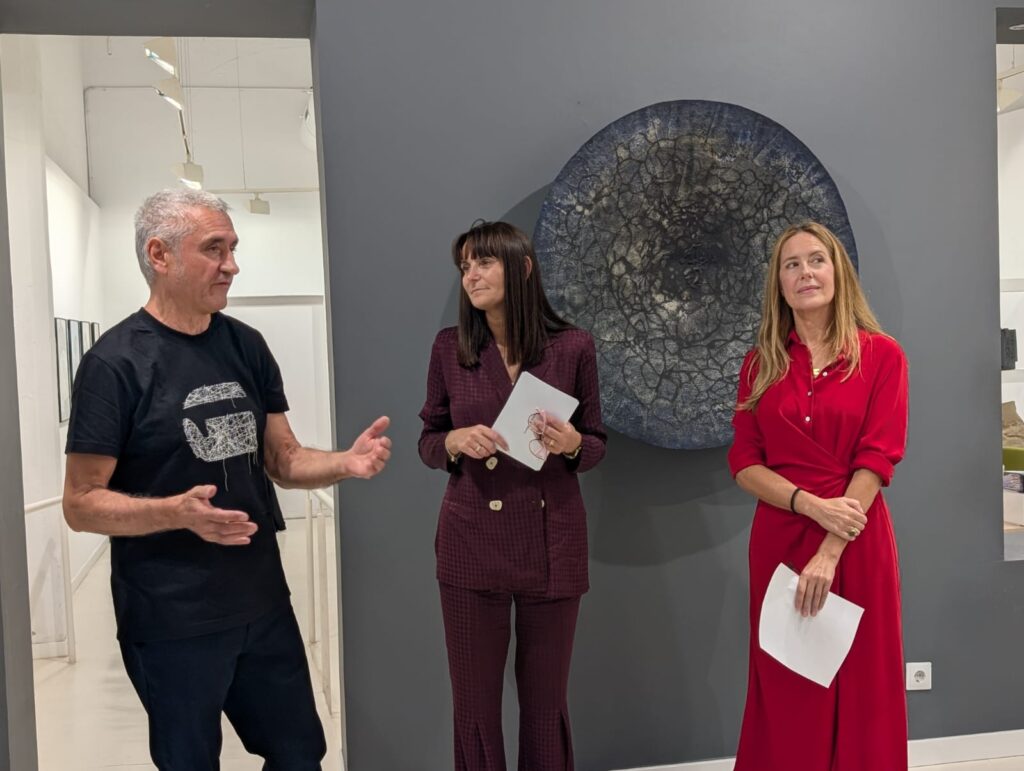 Tres personas están de pie frente a una obra circular en una galería.