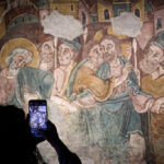 Una persona fotografía con su móvil una pintura mural medieval de Sant Esteve.