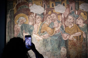 Una persona fotografía con su móvil una pintura mural medieval de Sant Esteve.